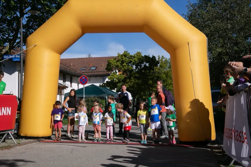 Die Jüngsten an der Startlinie unter dem Startbogen, daneben Eltern und Zuschauer.