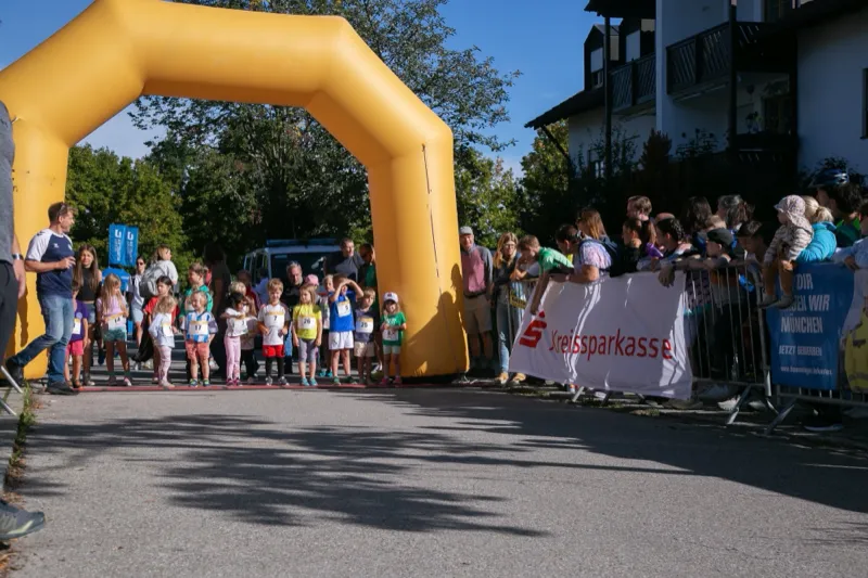 Kinder warten unter dem Startbogen auf den Start, dicht gedrängtes Publikum an der Absperrung.